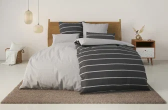 Ein bequemes Bett mit einer Wendebettwäsche in Grau-Weiß gestreiftem Design und einer Linon-Qualität.
