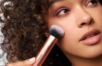 Eine Frau mit lockigem Haar hält einen Make-up-Pinsel an ihre Wange