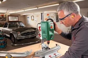 Ein Mann arbeitet an einer grünen Tischbohrmaschine in einer Werkstatt, im Hintergrund ein silberner Mercedes.
