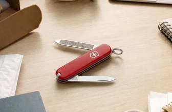 Rotes Victorinox Taschenmesser mit ausgezogenem Messer und Feile auf hellem Holztisch neben Laptop und Notizbuch