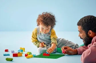 Vater und Kind bauen gemeinsam mit LEGO Duplo-Steinen auf einer grünen Bauplatte