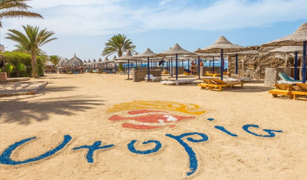 A Beach With Umbrellas And A Sign On Sand