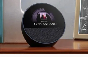 Schwarzer Amazon Echo Spot auf Holzregal, Display zeigt Uhrzeit 7:00 und Musiktitel Electric Soul von Sam.