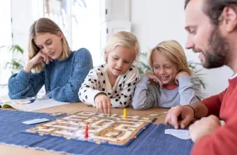 Familie spielt Brettspiel mit Labyrinth-Bahnen und bunten Figuren am Tisch