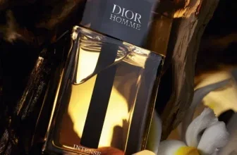 Dior Homme Intense Parfümflasche mit goldener Flüssigkeit, dunklem Deckel und weißer Irisblüte auf Holz.