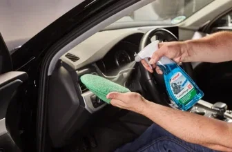 Ein Mann hält einen grünen Tuch und eine Reinigungssprayflasche in den Händen im Innenraum eines Autos.