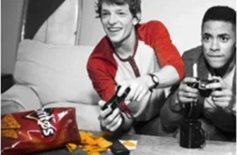 Zwei junge Männer spielen Videospiele, während auf dem Tisch eine rote Doritos-Tüte und Chips liegen.