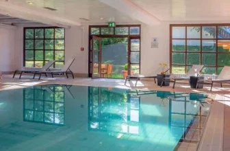 Innenpool mit Liegestühlen und großen Fenstern im Wellnessbereich