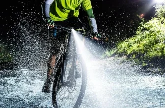 Mountainbiker in Neonkleidung fährt bei Nacht durch Wasser, das Fahrradlicht leuchtet stark.