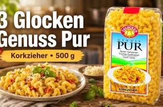 Eine Packung 3 Glocken Genuss Pur Korkzieher Nudeln neben einem Teller mit gekochten Nudeln, Tomaten und Basilikum auf einem Holztisch.