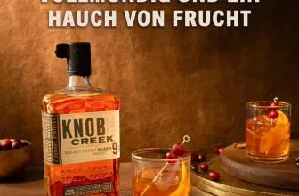 Knob Creek Whiskey-Flasche neben zwei Gläsern mit Cocktail, Eiswürfeln und Kirschen auf einem Holztisch.