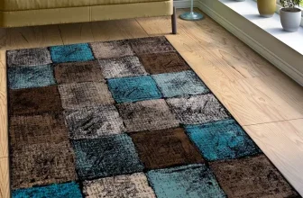 Teppich Metroplis mit quadratischem Muster in Blau, Braun und Grau auf hellem Parkettboden vor Sofa