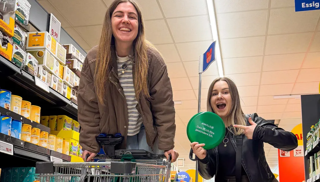Lidl AOK Aktion im Supermarkt: Zwei Frauen zeigen Fitness-Aktion und Rabatt-Möglichkeit beim Einkauf