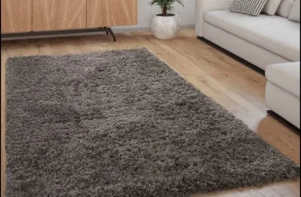Ein dunkelgrauer Hochflor-Teppich liegt auf einem Holzboden in einem Wohnzimmer.