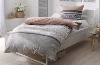 Ein weißes Bett mit grauer und rosa Bettwäsche und einem dekorativen Kissen.