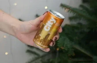 Eine Hand hält eine Dose City Sunrise Orange vor einem Weihnachtsbaum mit Lichterkette.