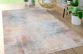Mehrfarbiger Teppich mit abstraktem Muster auf einer Holzterrasse neben einem Rattanhängesessel und Topfpflanzen.