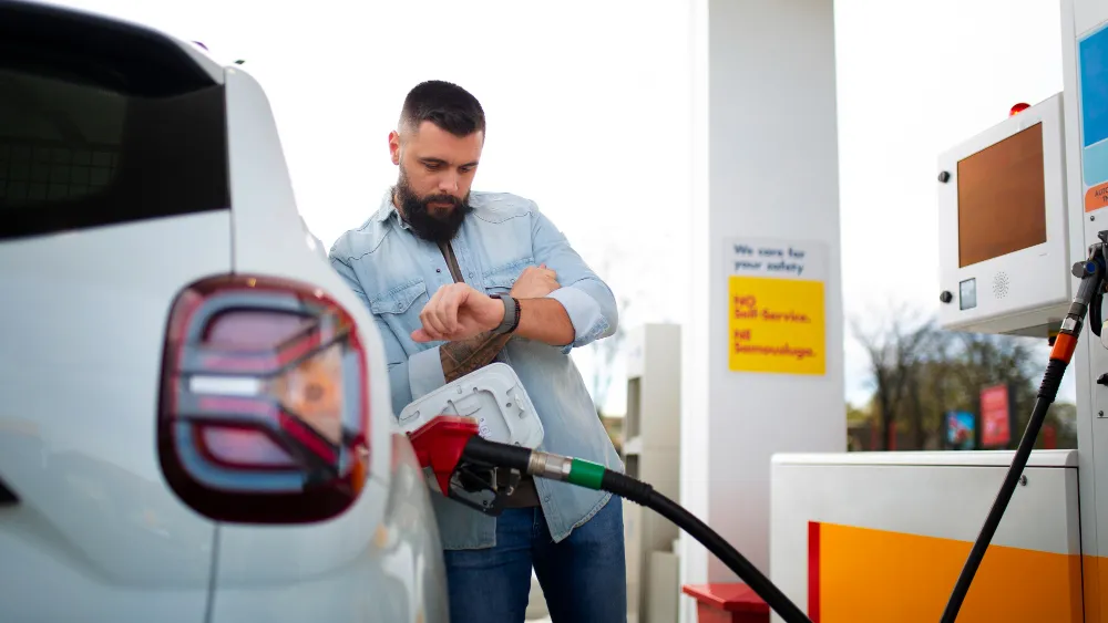Günstig tanken 2026: Autofahrer überprüft die Uhrzeit beim Tanken an einer modernen Tankstelle.