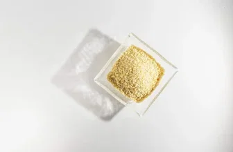 Ein Glas mit gelben Dinkelbröseln auf weißem Grund