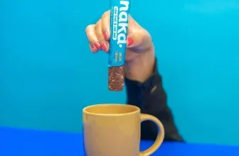 Hand hält Nākd Salted Caramel Riegel über gelben Becher vor blauem Hintergrund