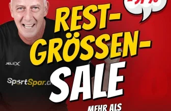 Ein älterer Mann mit kahlem Kopf und einem schwarzen T-Shirt lächelt in die Kamera, im Hintergrund ein rotes Plakat mit gelben und weißen Buchstaben.