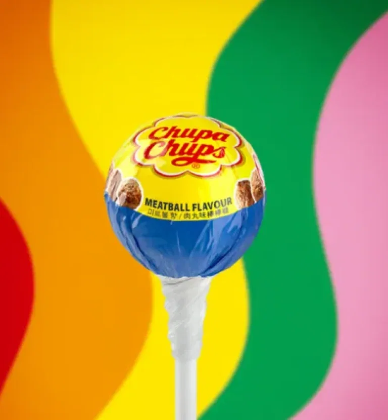 Ein Chupa Chups Lolli mit Köttbullar-Geschmack vor farbenfrohem Hintergrund