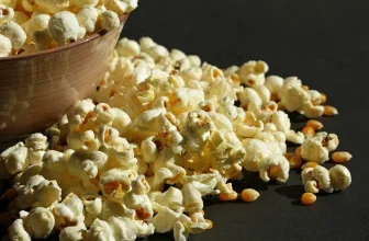 Ein Haufen Popcorn neben einer braunen Schale auf schwarzem Hintergrund