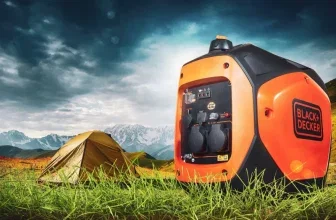 Ein orangefarbener und schwarzer Inverter-Stromgenerator von Black+Decker im Gras neben einem Zelt mit Bergen im Hintergrund.