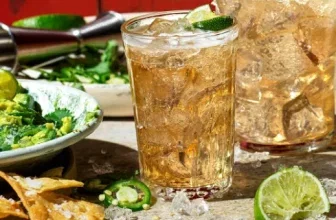 Ein Glas Rum-Cocktail mit Eis und Limette, daneben Tortilla-Chips und Guacamole