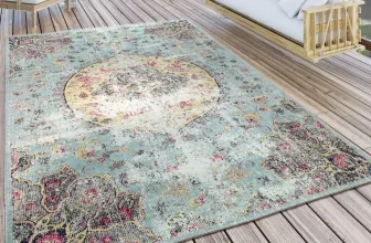 Blau-rosa Vintage-Teppich auf Holzterrasse neben weißer Hängematte und Gartenmöbeln