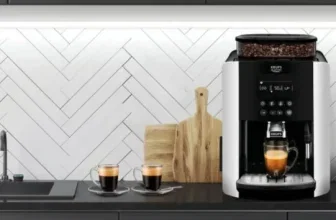 Ein KRUPS Kaffeevollautomat Arabica EA8178 auf einer Küchenarbeitsfläche neben zwei Kaffeetassen.