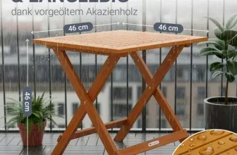 Ein klappbarer Holztisch aus Akazienholz steht auf einem Balkon während es regnet, daneben zwei Pflanzen.
