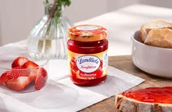 Ein Glas Erdbeerkonfitüre neben einer Schale mit frischen Erdbeeren und einer Scheibe Toast mit Konfitüre