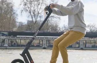 Ein Mann fährt auf einem schwarzen E-Scooter mit gelben Akzenten und kantigem Design neben einem Fluss.