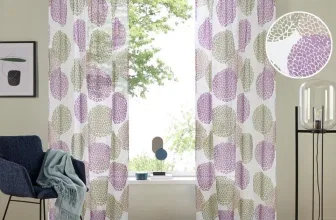 Ein Wohnzimmer mit einer Gardine, die ein Muster aus violetten und grünen Blättern aufweist, davor ein Sofa und ein Tisch.
