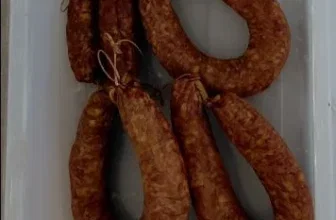 Ein Bild von geräucherten Wurstkränzen im Naturdarm mit rotem Clip und naturfarbenem Wurstgarn in einer weißen Schale.