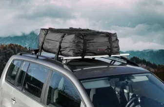 Ein silbernes Auto mit einer schwarzen Dachgepäckträgertasche, im Hintergrund eine Berglandschaft mit Wolken