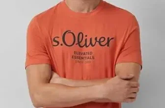Ein Mann mit kurzen braunen Haaren trägt ein oranges T-Shirt mit schwarzem Aufdruck und hat die Arme verschränkt.