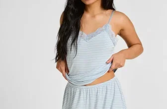 Eine junge Frau mit langen schwarzen Haaren trägt ein blau-weiß gestreiftes Pyjama-Set mit Spitze-Details.