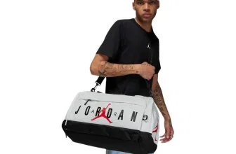 Ein Mann mit kurzem Haar und tätowierten Armen hält eine weiße und schwarze Sporttasche mit dem Jordan-Logo.