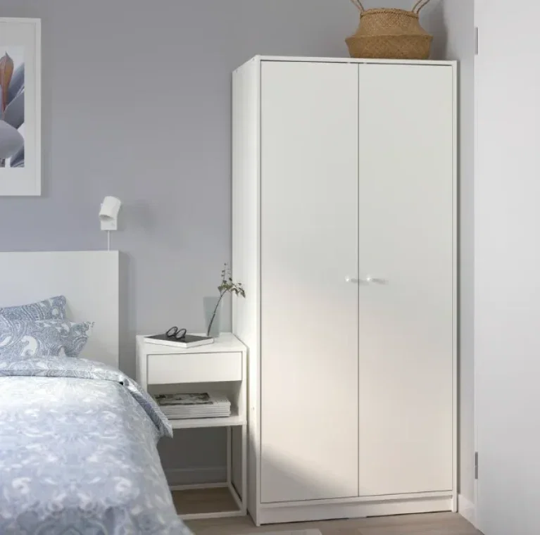 Weißer Kleiderschrank mit zwei Türen, daneben ein Bett und ein Nachttisch