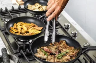 Ein Küchenhand mit einer Grillzange greift in eine Pfanne mit gebratenem Lamm, zwei weitere Pfannen mit Kartoffeln und Pilzen stehen auf dem Herd.