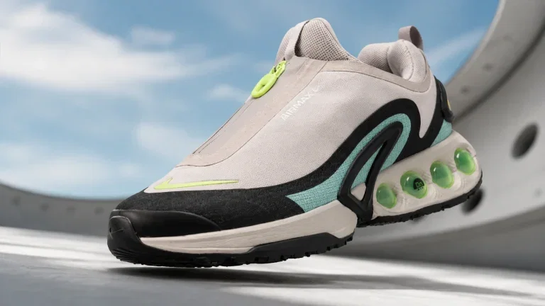 Ein Nike Air Max DN Schuh in Grau, Schwarz, Blau und Gelb auf grauem Untergrund vor blauem Himmel