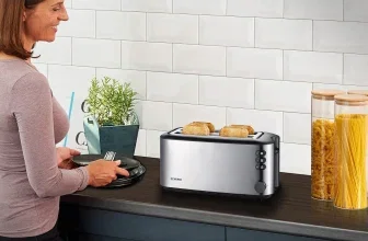 Eine Frau steht an der Küchenzeile und schaut auf einen Toaster mit vier Brotscheiben und Brötchenaufsatz.