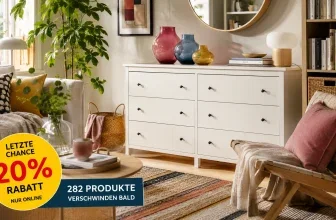 Ein hell erleuchtetes Wohnzimmer mit Sofa, Sessel, Kommode und Bücherregal. Im Vordergrund ein runder Tisch mit Dekorationen. Rechts ein Sessel mit Kissen und Decke.