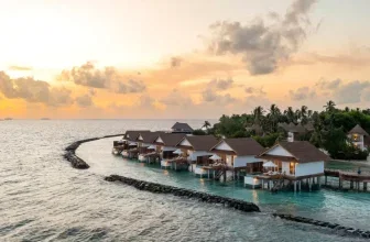 Luftaufnahme von Bungalows auf Pfählen über türkisfarbenem Wasser bei Sonnenuntergang