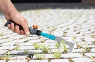 Hand hält Gardena Fugenkratzer und entfernt Unkraut aus Pflastersteinen