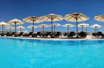 Blauer Pool mit Sonnenliegen und weißen Sonnenschirmen am Gorgonia Beach Resort
