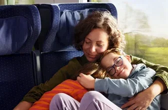 Mutter und Kind schlafen kuschelnd auf blauen Zugsitzen neben dem Fenster