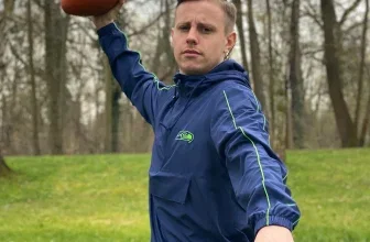 Mann in blauer Jacke hält JELEX American Football hoch im Wald